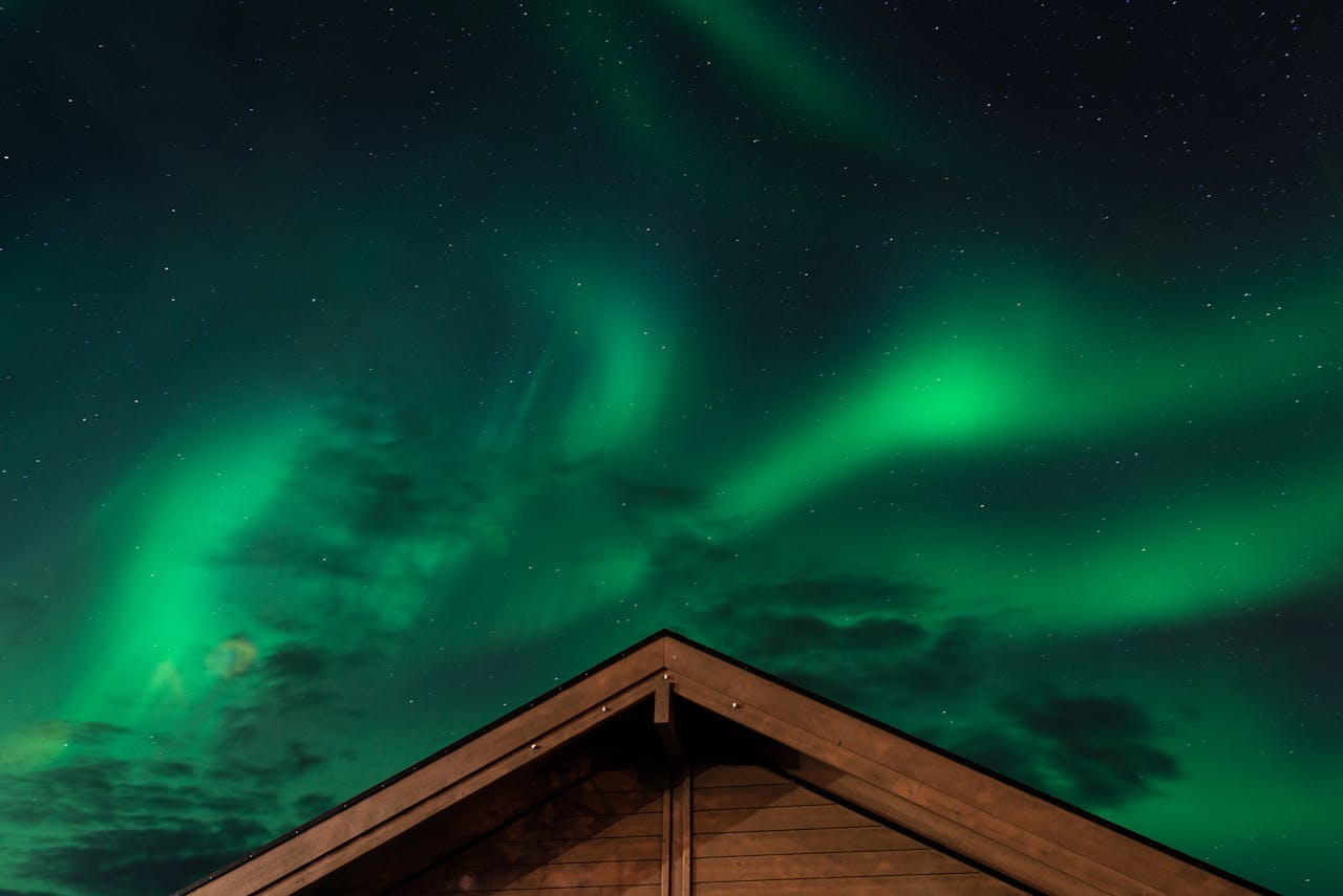 Stunning view of the Northern Lights over a cabin roof under a starry night sky.